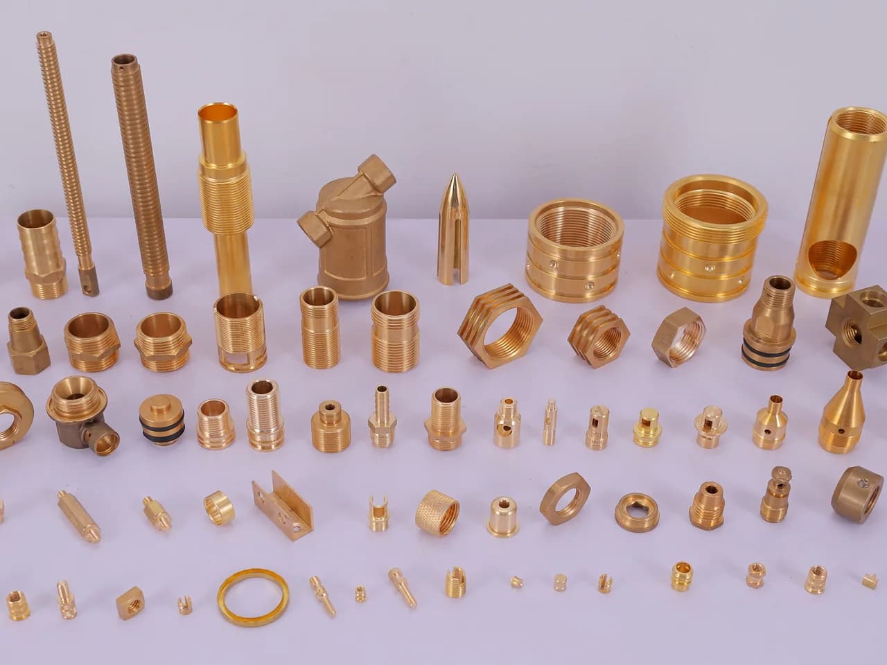 The full range of turned brass parts — threaded studs, hex nipples, bushes, nozzles and pins laid out on the studio table