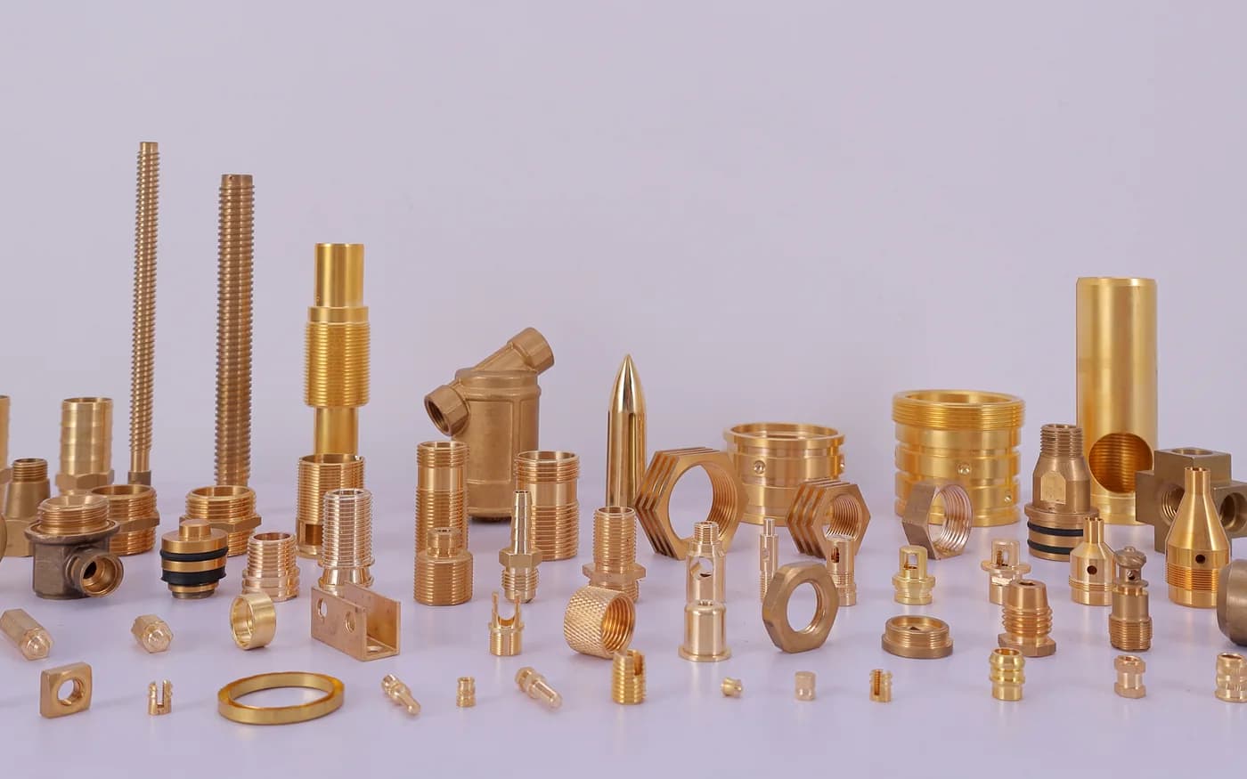 The full range of turned brass parts — threaded studs, hex nipples, bushes, nozzles and pins laid out on the studio table