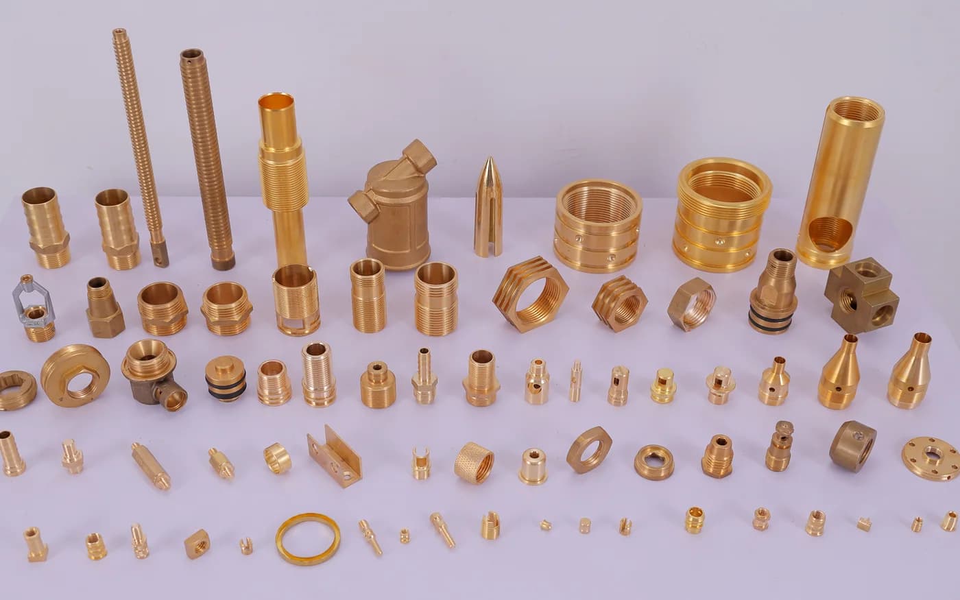 The full range of turned brass parts — threaded studs, hex nipples, bushes, nozzles and pins laid out on the studio table