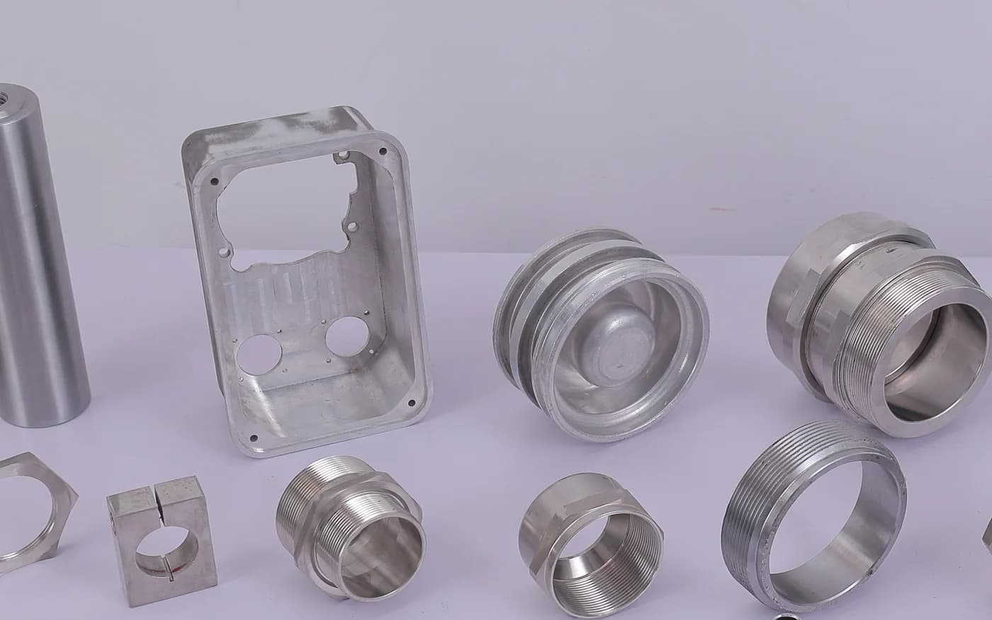 Machined stainless plate with cut-outs beside turned rings, a shaft and a threaded ring
