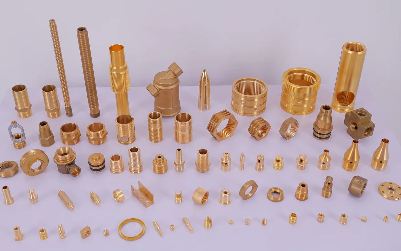The full range of turned brass parts — threaded studs, hex nipples, bushes, nozzles and pins laid out on the studio table